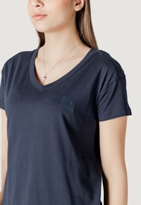 T-shirt v-neck navy a maniche corte, realizzato in cotone morbido, con una piccola etichetta logo sul petto. Texture liscia, design casual.