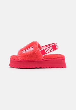 Sandale plateforme rouge duveteuse avec bout ouvert et bande arrière élastique de marque, logo UGG visible sur le côté et la semelle.