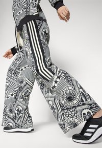 Μαύρο και άσπρο patterned παντελόνι σε ίσιο σχέδιο με περίπλοκα σχέδια, τρεις κατακόρυφες ρίγες στο πλάι και συνδυασμένο με μαύρα αθλητικά παπούτσια.