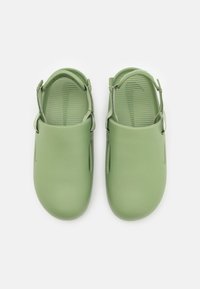Paire de sabots vert clair à enfiler avec semelles intérieures texturées et brides de talon réglables sur fond blanc.