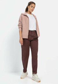 Light pink ribbed cardigan with a zip collar, white t-shirt, and burgundy tapered pants, paired with beige sneakers. Casual outfit details noted.