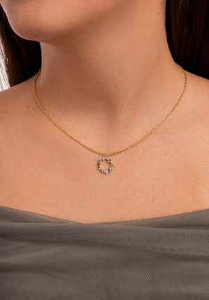 Collar de cadena de oro con un colgante circular adornado con piedras preciosas de colores variados, incluyendo púrpura, rosa y azul, sobre un fondo neutro.