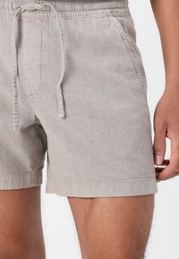 Shorts en lin beige avec une taille élastique, fermeture à cordon de serrage et poches latérales. Le tissu a une finition texturée et une coupe ajustée.