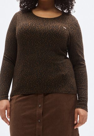 Woman wearing a brown and black leopard print long-sleeve top with a brown buttoned corduroy skirt.