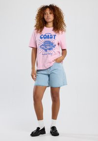 Pink short-sleeve t-shirt with blue graphic print of a fish and text "CALIFORNIA COAST CATCH OF THE DAY," paired with light blue denim shorts.