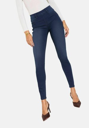 Blugi skinny cu talie înaltă, de culoare albastru închis, cu o textură netedă și croială strâmtă, asortați cu pantofi maro cu toc înalt.