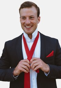 Cravatta e fazzoletto da taschino a motivi rossi con una camicia bianca e un blazer nero. La persona sta sistemando la cravatta con un'espressione sorridente.