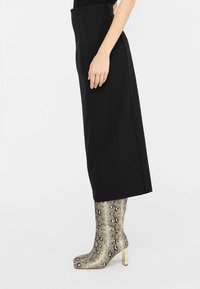 Schwarze hochgeschnittene Hosen mit geradem Schnitt, kombiniert mit glänzenden, metallischen Ankle Boots im Schlangenhaut-Muster und Blockabsatz.