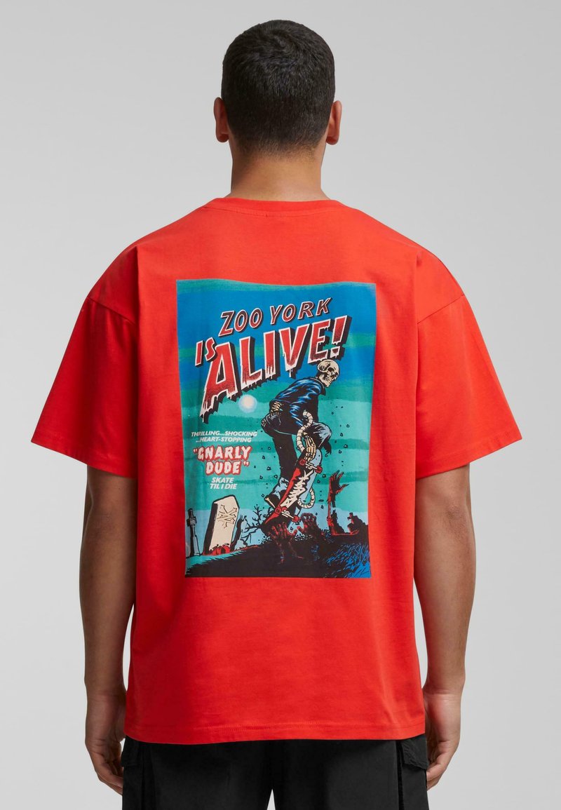Rød bomulds t-shirt med grafisk print på ryggen. Designet inkluderer teksten "ZOO YORK IS ALIVE!" sammen med en illustreret scene i blå og sort.