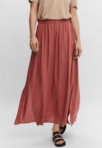 Lange, vloeiende rok van stof in stofroze met een elastische tailleband en een zijsplits, gecombineerd met zwarte sandalen en een beige top.
