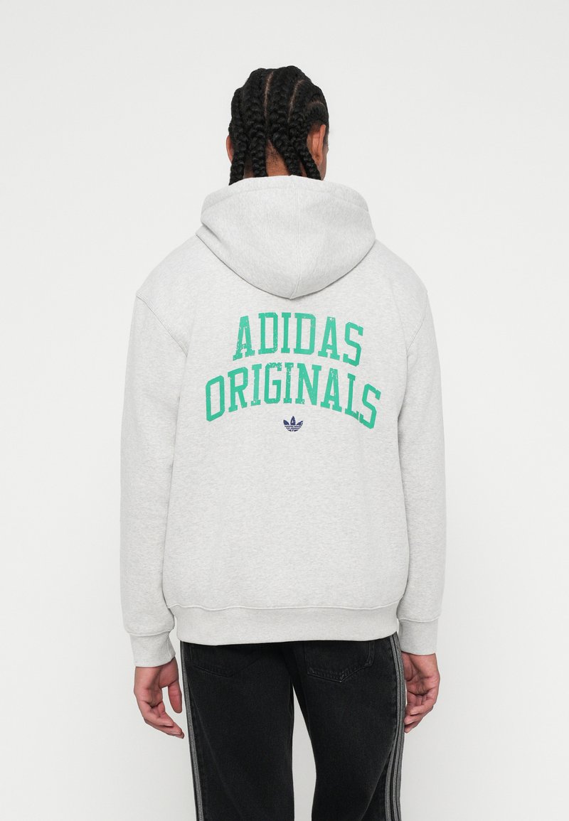 Grå hættetrøje med "ADIDAS ORIGINALS" i grøn skrift på ryggen, med et logo nedenunder. Tekstiler med struktur og en afslappet pasform.
