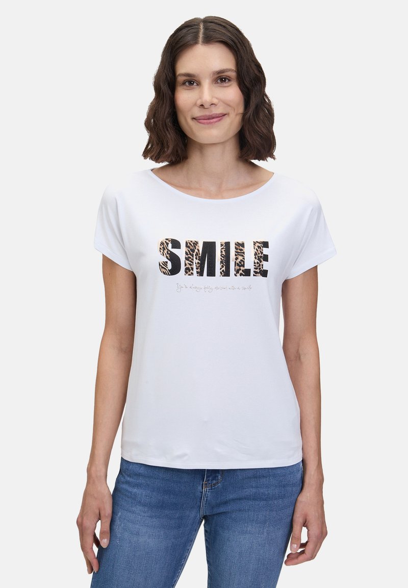 T-shirt blanc à manches courtes avec le texte "SMILE" en noir et imprimé animal. Encolure ronde et coupe décontractée, fabriqué en coton doux.