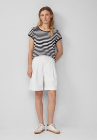Czarno-biała, pasek krótki top z krótkim rękawem, w zestawie z białymi szortami do kolan i jasnymi trampkami, charakteryzujący się luźnym krojem i odwiniętymi brzegami.