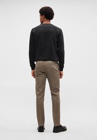 Musta collegepaita, khakinväriset housut, sileää puuvillakangasta, tavallinen istuvuus, resorireunaiset hihansuut, kaksi vetoketjullista takataskua, mustat kengät.