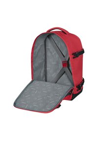 Punainen reppu, jossa on vetoketjulla suljettava aukko, harmaa vuori toistuvalla kuviolla, sisäiset hihnat tavaroiden kiinnittämiseen ja säädettävät sivulukot.