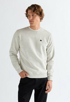 Jasnoszara bluza z okrągłym dekoltem, ściągaczami na mankietach i dole. Na piersi małe czarne logo. Miękka w dotyku, casualowy design.