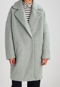 Cappotto oversize in verde menta, morbido, con colletto a revers, maniche lunghe e tasche laterali, realizzato in tessuto testurizzato.