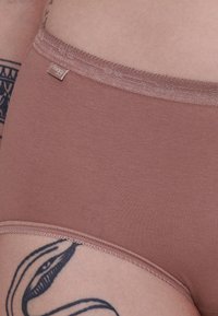 Bruine katoenen boxershort met een gladde textuur, voorzien van een subtiele, glanzende tailleband en een klein label. Close-upweergave met huid en tattoo op de achtergrond.