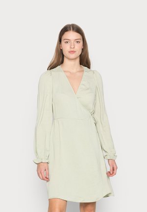 Vestido envolvente verde claro com mangas bufantes longas, decote em V profundo, detalhe de laço na cintura e um corte descontraído, feito de um tecido leve e macio.