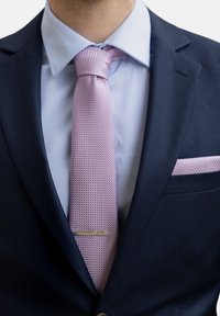 Dunkelblaues Sakko mit einem hellblauen Hemd und einer strukturierten pinken Krawatte. Die Krawatte wird von einer kleinen silbernen Krawattennadel begleitet und einem Einstecktuch mit einem ähnlichen Muster.