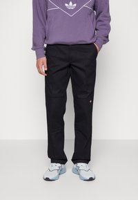 Svarta byxor med rak passform, med sidofickor och diskreta paneldetaljer, kombinerade med en lila hoodie och blå sneakers.