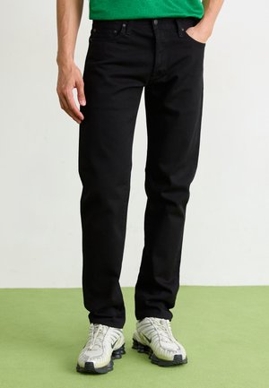 Zwarte denim jeans met een rechte snit, voorzien van subtiele stiksels en vijf zakken, gecombineerd met wit-grijze sneakers.
