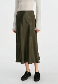 Sukienka midi w oliwkowym satynowym kolorze o gładkiej teksturze, z bocznym rozcięciem i subtelnym metalicznym akcentem. Zestawiona z czarnymi, sznurowanymi trampkami.