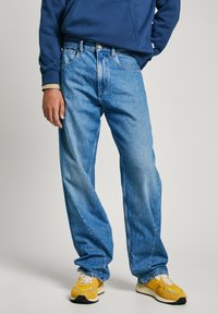 Lichtblauwe, losvallende denim jeans met vervaging, vijf-pocket ontwerp en een gouden knoopsluiting. Draag ze met gele sneakers en een marineblauwe hoodie.