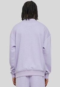 Sweatshirt lilas avec un col rond, des épaules tombantes, des poignets et un ourlet côtelés, et une texture en coton lisse. Vue de dos.