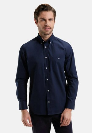 Chemise à manches longues bleu marine avec un col boutonné, des boutons blancs et une poche poitrine. Fabriquée en tissu lisse ; coupe ajustée.