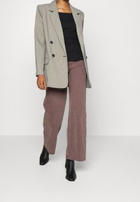 Blazer doppiopetto a quadri grigi, top aderente nero e pantaloni a gamba larga rosa antico, abbinati a stivali neri con tacco. Texture morbide, design strutturato.