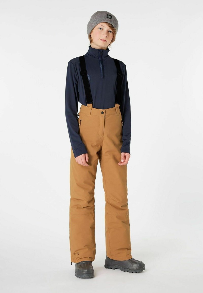 Pantaloni da neve beige con bretelle nere regolabili, abbinati a una maglietta a maniche lunghe scura. Berretto grigio lavorato a maglia, dalla texture liscia e dal fit rilassato.