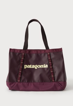 Σκούρα μωβ τσάντα Patagonia με διπλούς ιμάντες ώμου και λογότυπο τυπωμένο σε κρεμ χρώμα στο κέντρο μπροστά πάνω σε μονόχρωμο φόντο.