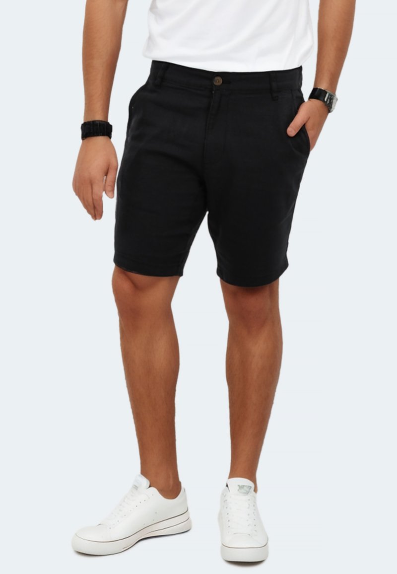 Black shorts with a smooth cotton fabric, a button closure, side pockets, and a straight cut. Paired with white sneakers for a casual look.