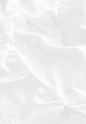Vit tyg med texturerad broderi i ett blommönster, med mjuka veck och draperingar som framhäver ett slätt, lätt material.