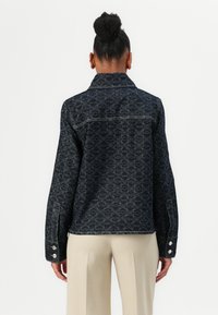 Mørkeblå denimjakke med geometrisk mønster, kontrasterende sømmer og trykknapper på ermene. Rett snitt.