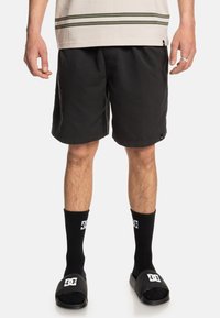 Black swim shorts made of lightweight fabric, featuring a flat waistband. Paired with black socks and slide sandals with logo accents.