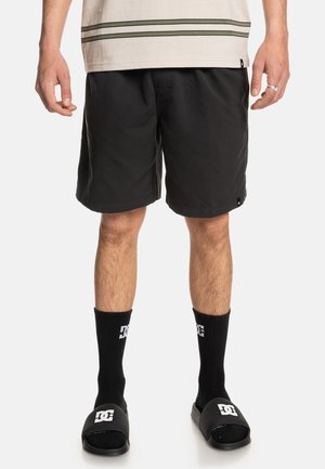 Black swim shorts made of lightweight fabric, featuring a flat waistband. Paired with black socks and slide sandals with logo accents.