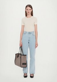 Beige nauwsluitend T-shirt, lichtblauwe high-waisted jeans, zwarte platte schoenen en een grote grijze draagtas met zwarte afwerking en logo.