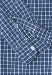Modrá námornícka a biela kockovaná košeľa s dlhými rukávmi, gombíkmi na manžetách a hladkým bavlneným materiálom. Má malé gombíky a kontrastné detaily.