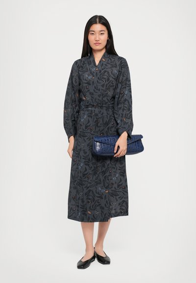 Long-sleeve, dark gray dress with floral pattern, cinched waist, and ankle length; paired with a blue crocodile-embossed clutch and black flats.