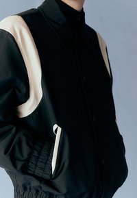 Czarna kurtka z kremowymi akcentami, z kołnierzem, zapięciem na guziki, elastycznymi mankietami i bocznymi kieszeniami. Gładka faktura tkaniny.