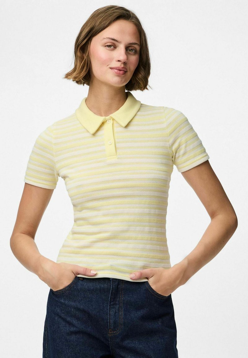 Svetlo rumena polo majica s prugami, kratkimi rokavi in mehkimi ovratnikom. Material izgleda teksturirano z oprijetim dizajnom. Uparjena z temno denim spodnjimi hlačami.