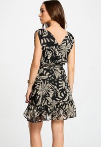 Zwarte jurk met bloemenpatroon in beige, met een V-achterkant, korte mouwen en een rucheszoom. Gemaakt van lichtgewicht stof.