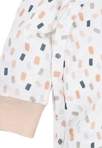 Witte babykleding met meerkleurige rechthoekige stippen, beige manchetten en witte drukknoopjes die langs de voorkant lopen.
