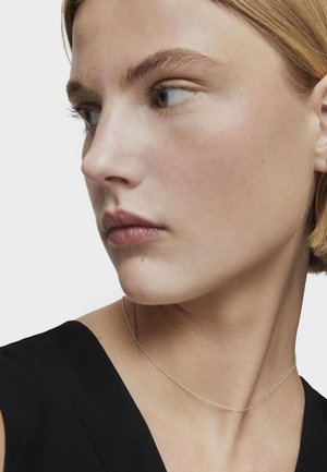 Collana in argento appoggiata sulla clavicola, con un design delicato e una texture liscia, presentata su una maglietta nera.