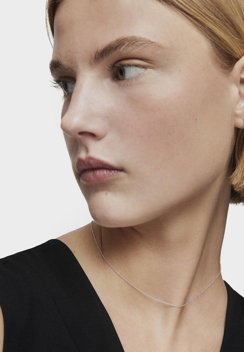 Collana in argento appoggiata sulla clavicola, con un design delicato e una texture liscia, presentata su una maglietta nera.