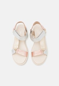 Sandalias planas con tiras metálicas en plata, oro rosa y beige. Suela lisa con correa ajustable en el tobillo y detalles texturizados.