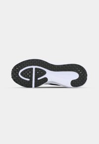 Semelle d’une chaussure de sport noire et blanche avec des motifs de grip texturés et un design segmenté pour la flexibilité et la traction.