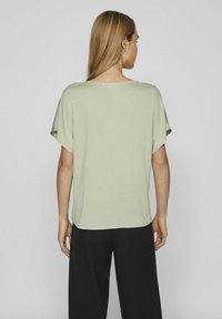 Top verde chiaro a maniche corte con una vestibilità rilassata e orlo arrotondato, abbinato a pantaloni neri a gamba larga. Texture liscia con dettagli minimi.